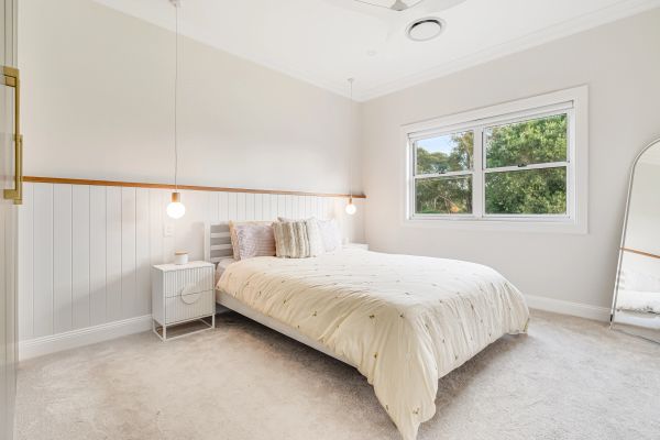 Minimalist bedroom with a cozy bed, hanging pendant lights, and a large window.