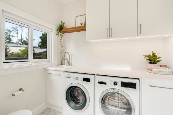 Bright laundry room with washing machine, dryer, and white cabinetry.