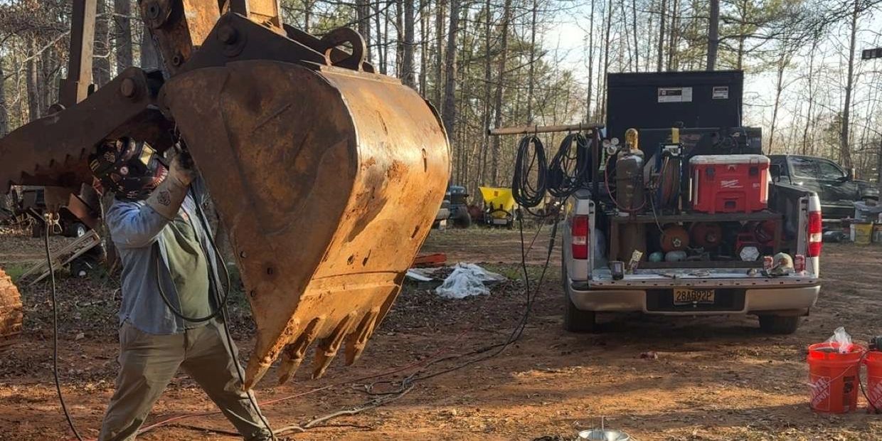Man welding on excavator bucket outdoors.