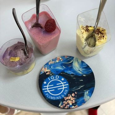 Three dessert cups with spoons and a GD Plumbing &amp; Air coaster.