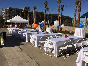 Outdoor event setup with tables, chairs, and colorful balloons.