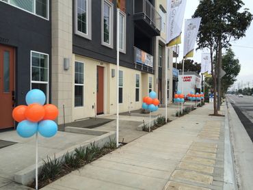 Colorful balloons line the sidewalk outside a modern building.