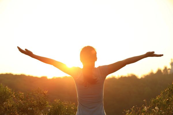 The image depicts a person standing with their arms outstretched, facing a bright sun.