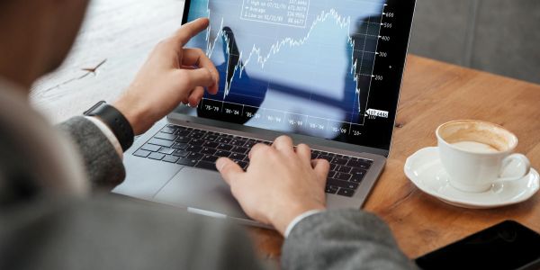 Person analyzing stock market graph on laptop with coffee nearby.