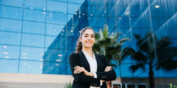 Confident young businesswoman standing outside a modern glass office building.