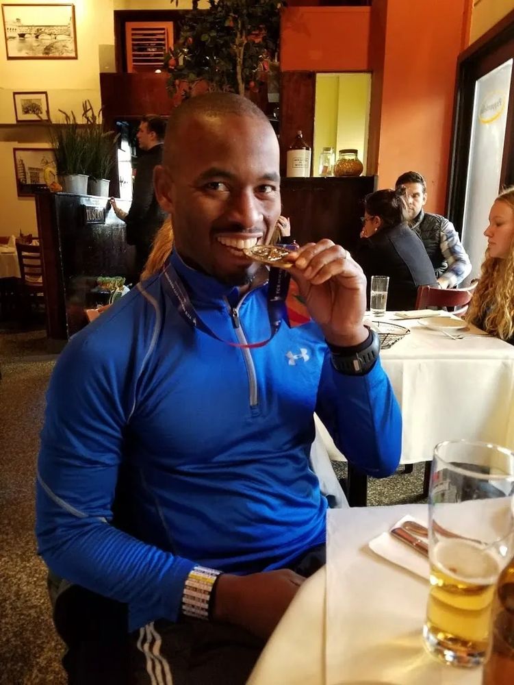 Wayne Johnson, a nutrition coach, smiling while biting his medal.
