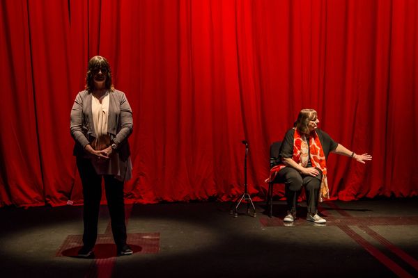 In front of a red curtain are performers Heather Lawson and Michelle Stevens standing in two pools o