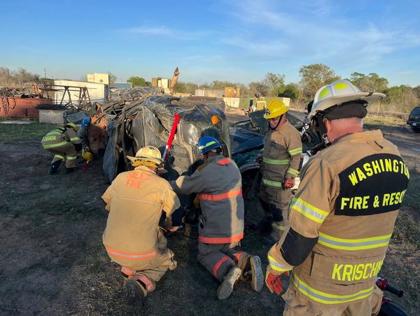 Firefighters in protective gear rescue at a flipped vehicle scene.