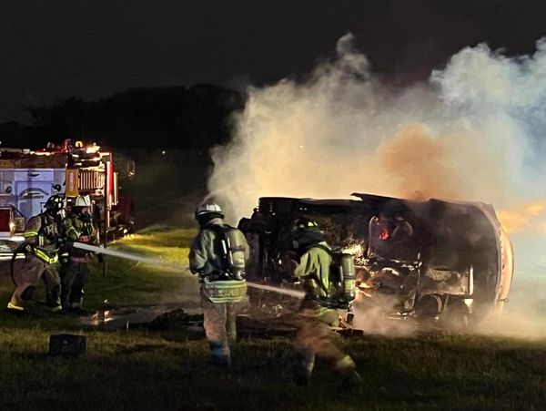 Firefighters extinguish a car fire at night with heavy smoke.