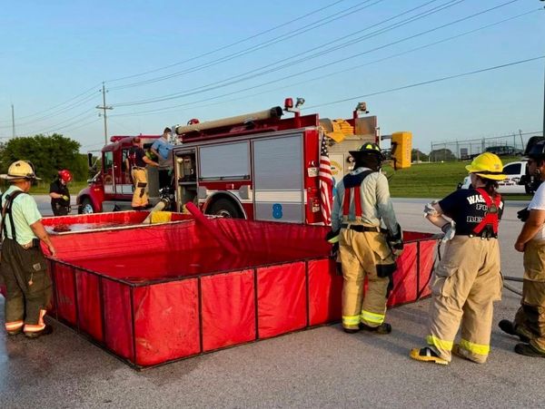 Firefighters set up a portable water tank near a fire truck.
