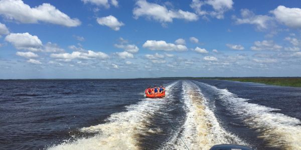 Three people tubing on a lake under a partly cloudy sky.