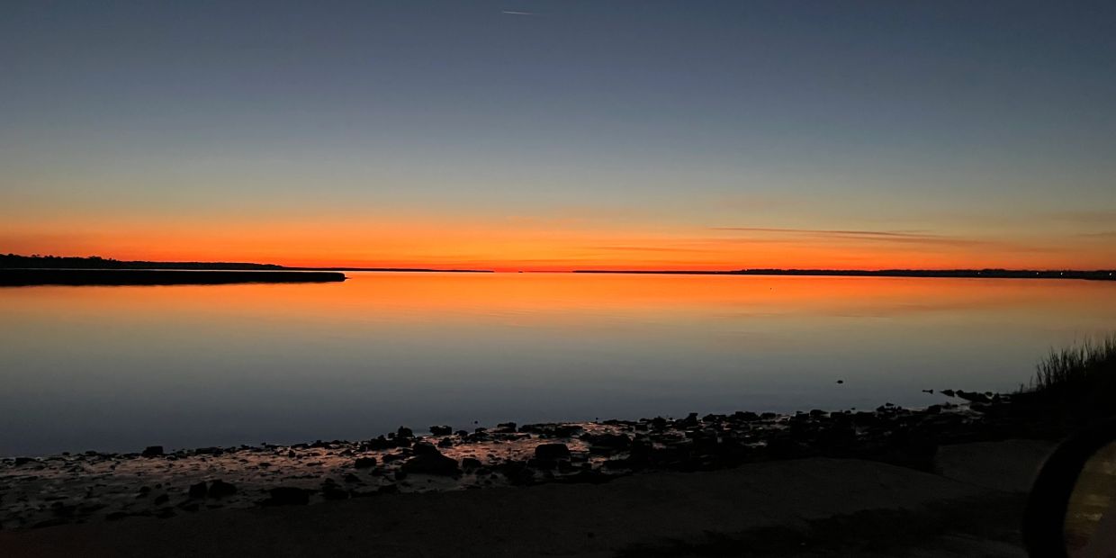 Serene sunset over calm water with a clear horizon.