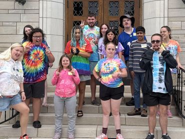 A diverse group of people posing on steps, many wearing colorful tie-dye shirts.