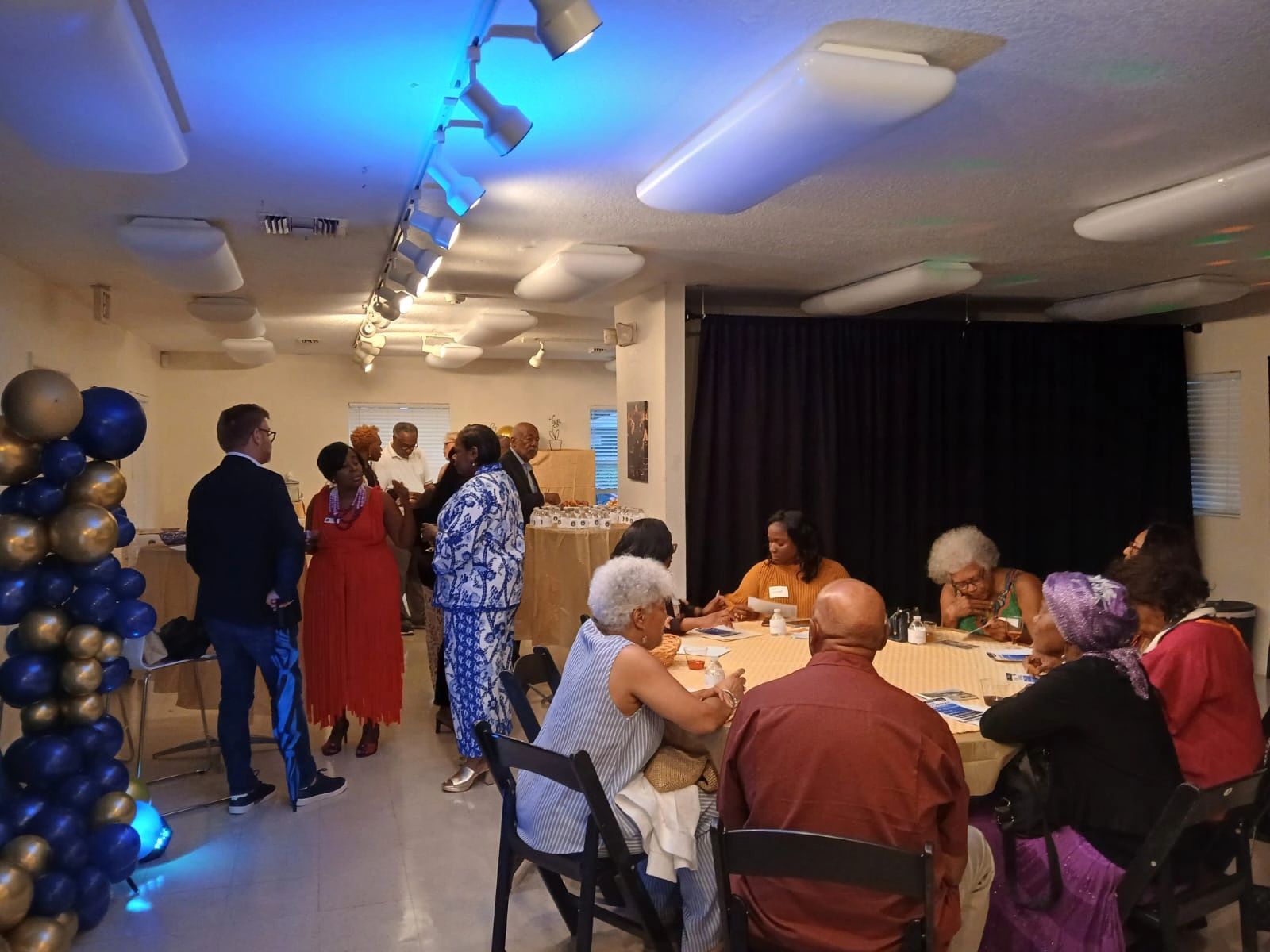 People socializing and seated at tables in a decorated indoor event space.