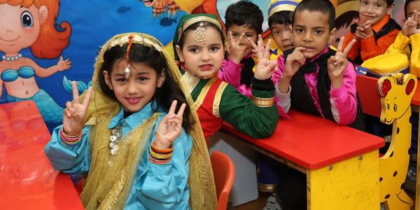 Children in colorful costumes making peace signs in a classroom.
