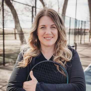 Smiling woman holding a tennis racket on an outdoor court.
