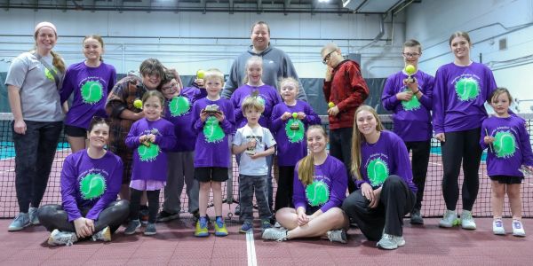 Group photo of children and adults on a tennis court.