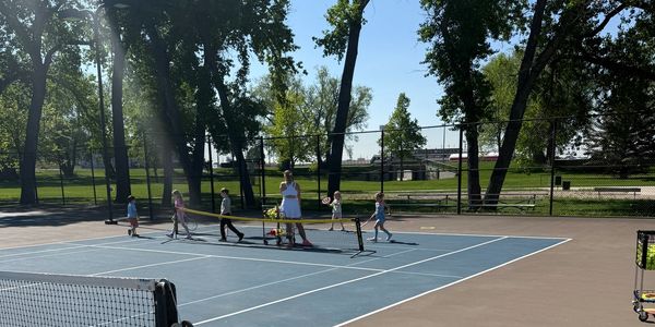 Children playing tennis on an outdoor court with an instructor.