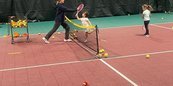 Adult teaching kids tennis on indoor court.