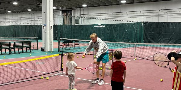 Adult teaching children tennis indoors.