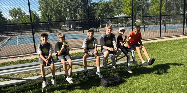 Six boys sitting on bleachers at a park on a sunny day.
