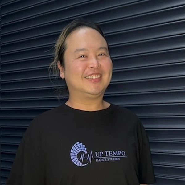 Person smiling in a black "Up Tempo Dance Studios" t-shirt with a tattooed arm.