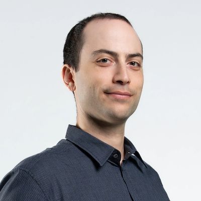 Smiling man in dark shirt against plain background.