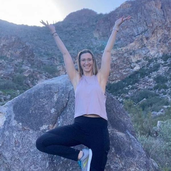 Woman doing yoga pose outdoors with mountains behind.