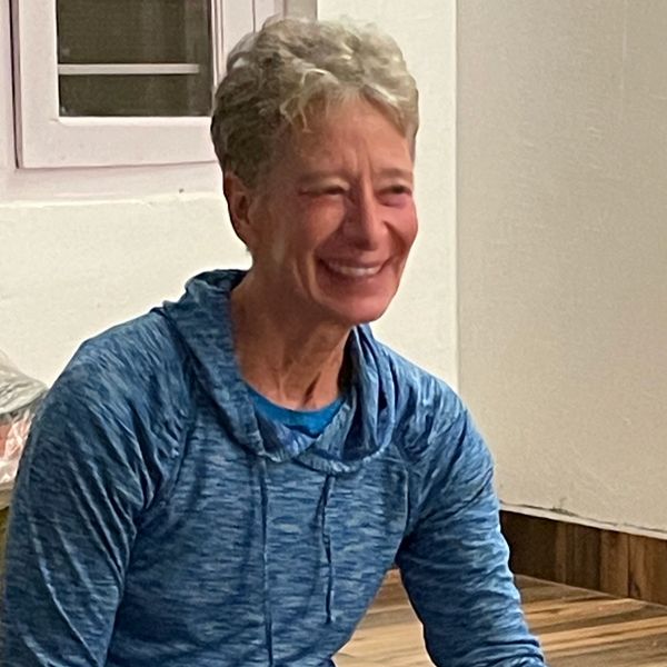 A smiling person in a blue hoodie sitting indoors.