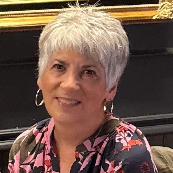 Smiling woman with short white hair and floral blouse.