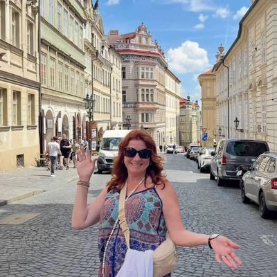 A woman happily poses on a sunny European cobblestone street.