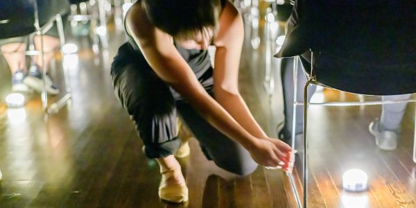 Person cleaning or adjusting something near a chair on a wooden floor.