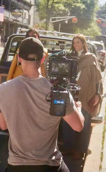 Cameraman filming two women outdoors on a sunny day.