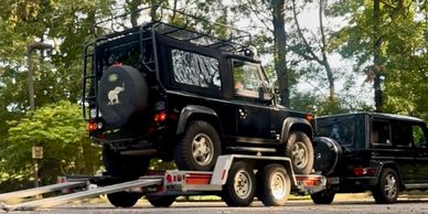 Black vehicle loaded on a trailer with another black SUV nearby.