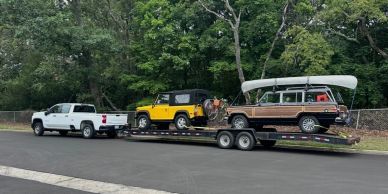 Pick-up truck towing trailer with two SUVs in wooded area.