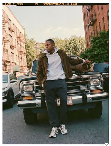 Young man leaning on a vintage SUV on a city street.