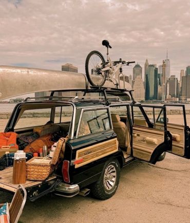 Vintage SUV packed for a trip with a bike on the roof near a city skyline.