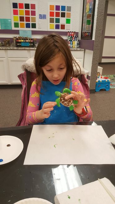 Young girl painting a small turtle model.