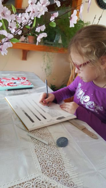 Young girl drawing at a table with flowers nearby.