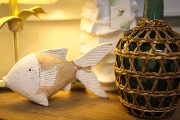 Decorative fish sculpture and woven bottle on wooden surface.