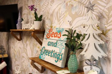 Decorative shelves with a tropical wallpaper, plants, and a festive sign.