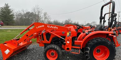 Orange Kubota tractor with front loader on gravel.