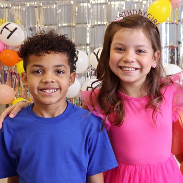 Two children smiling at a birthday party with festive decorations.