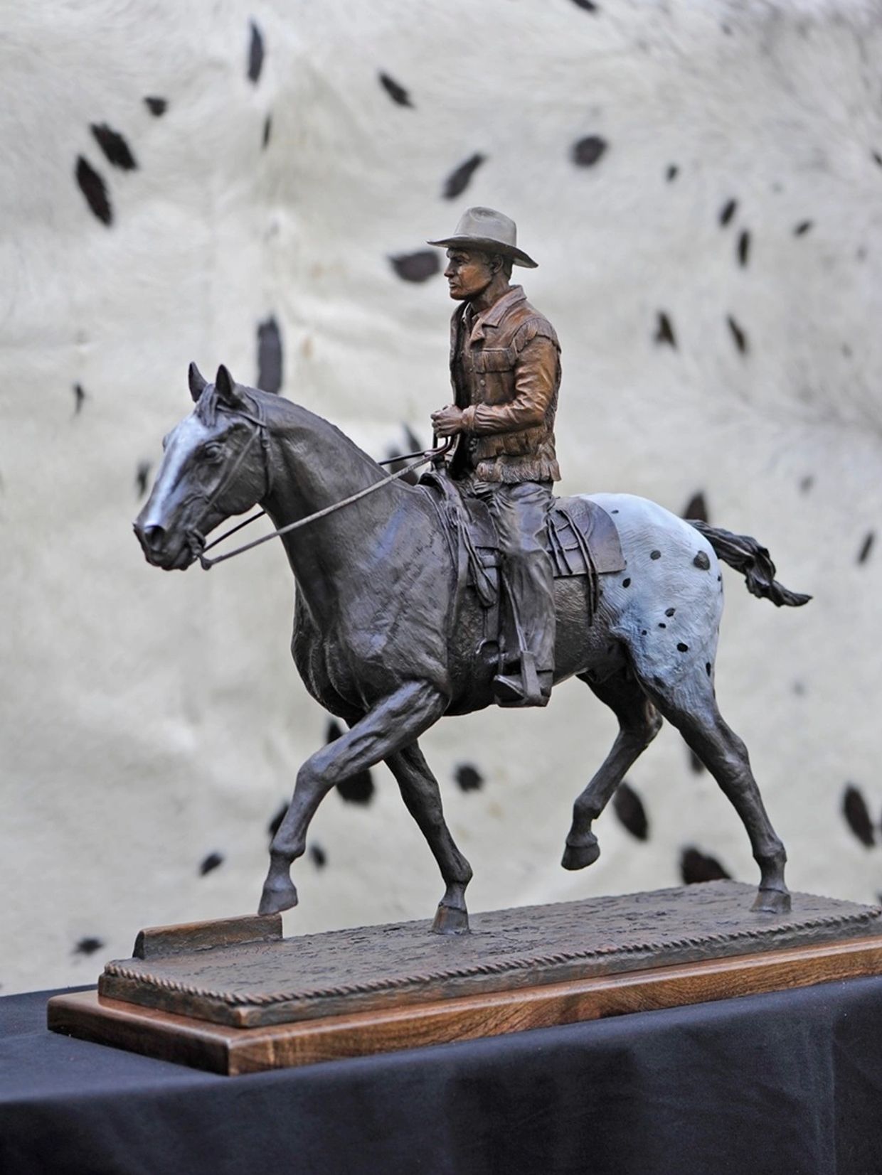 Bronze cowboy statue riding a spotted horse.