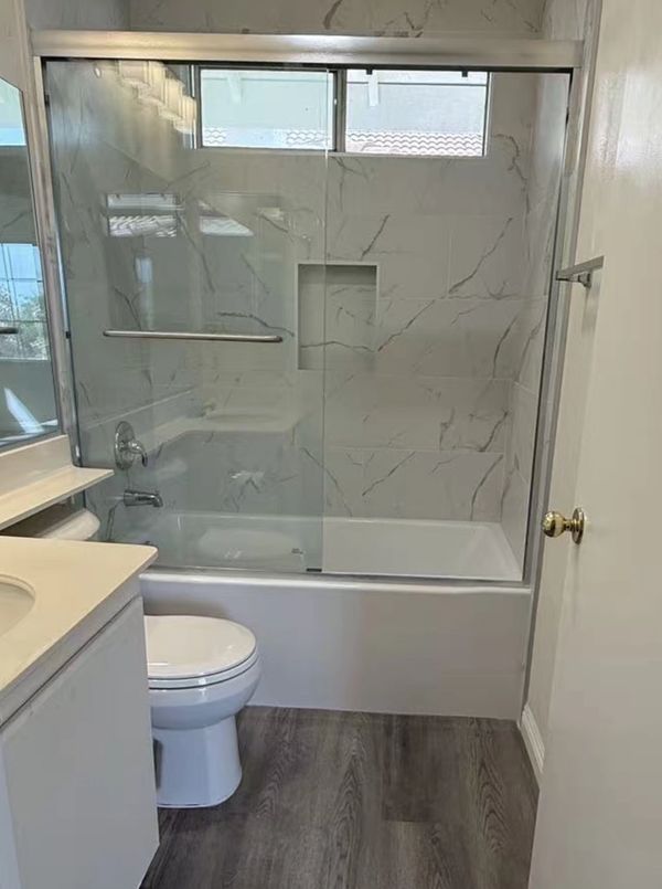 Modern bathroom with marble tiles, glass shower door, and wood-look flooring.