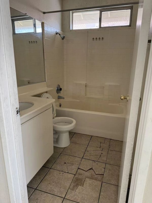 Bathroom with cracked tile floor, white bathtub, toilet, and sink under a large mirror.
