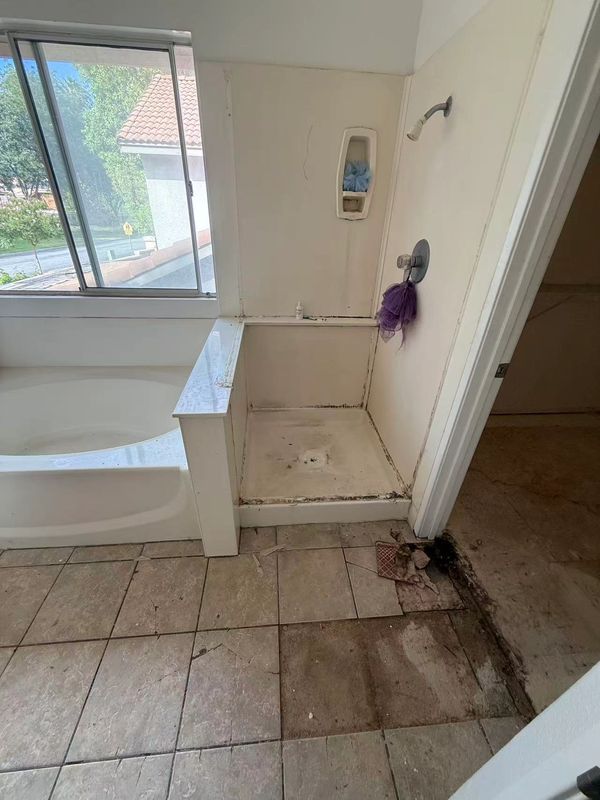 Bathroom with dirty shower area and stained floor tiles.