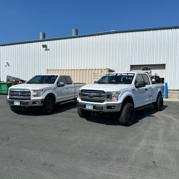 Two white Ford trucks parked outside an industrial building on a sunny day.