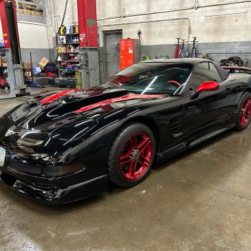Black sports car with red accents and rims in a garage.