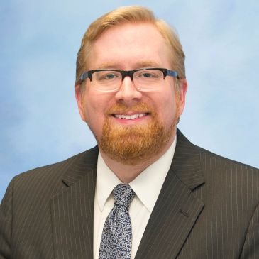 Smiling man with glasses and beard in suit.